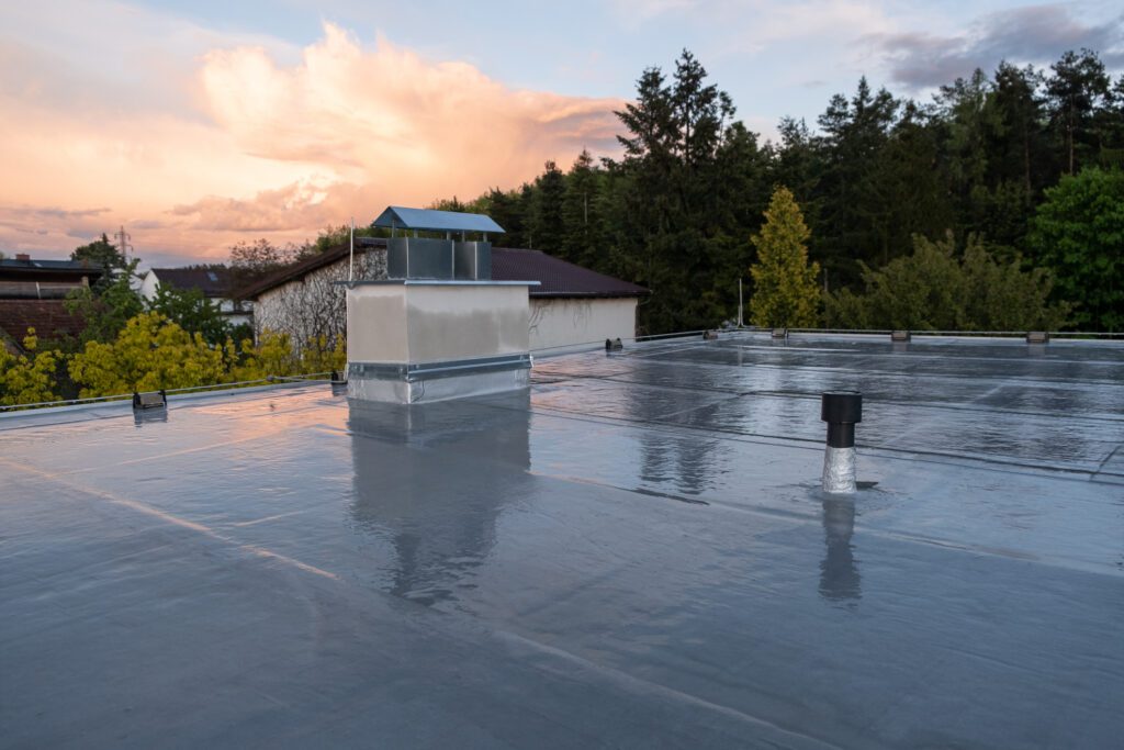 Flat roof covered with bitumen membrane and silver lacquer with chimney on a private house Reflections after rain