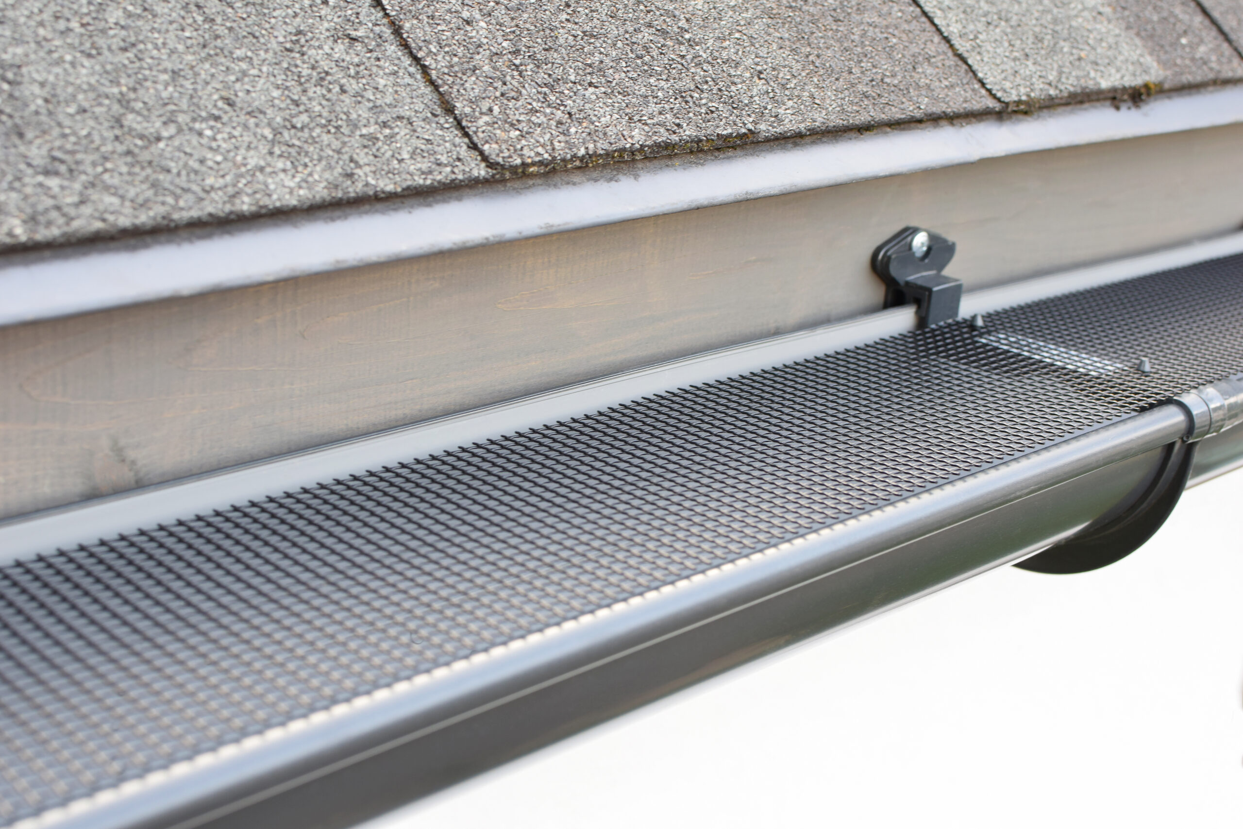 Plastic guard over new dark grey plastic rain gutter on asphalt shingles roof at shallow depth of field